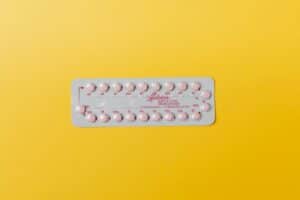 Plaquette de pilule contraceptive posée sur une table blanche avec verre d'eau, contexte santé féminine