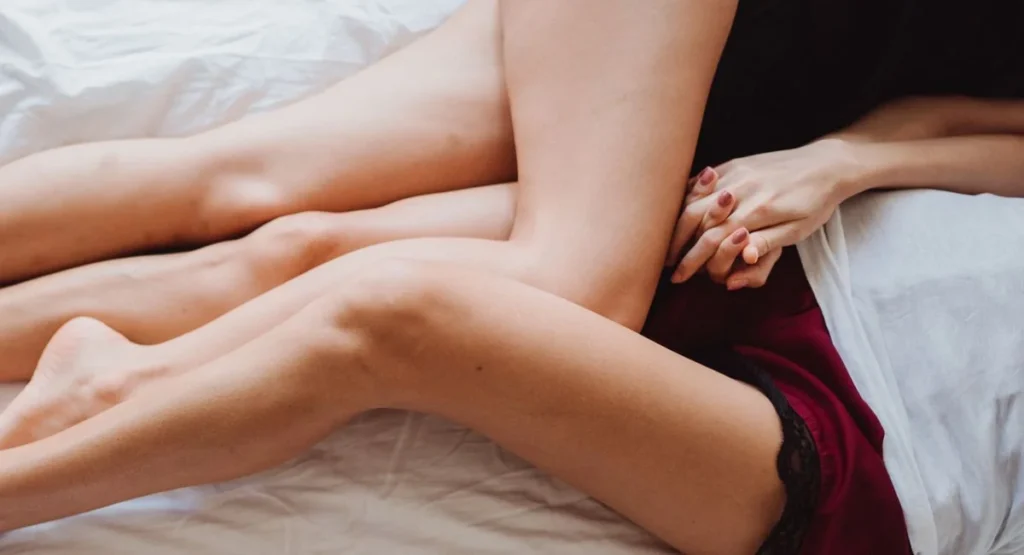 Femme allongée sur draps clairs observant sa vulve, lumière douce
