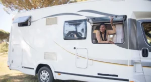 Femme seule devant son camping-car, matin, carnet à la main, nature sauvage