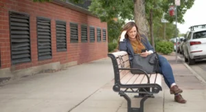 Femme seule sur un banc, regard tourné vers l’horizon, rue en arrière-plan