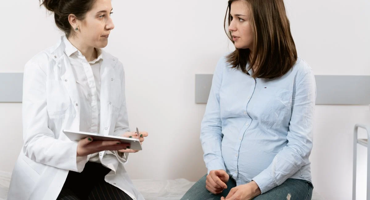 A pregnant woman consulting with a female doctor in a medical clinic setting.