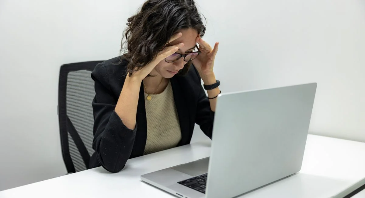 A young woman experiencing stress and fatigue while working on her laptop in an office setting.