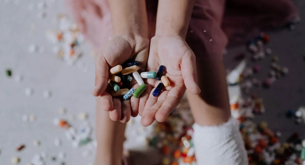 Close-up of a child holding pills with an injured leg in a cast, symbolizing health and recovery.