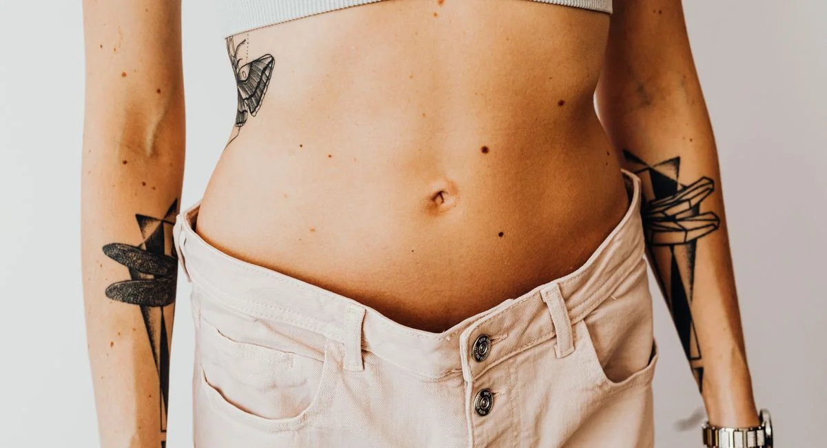 Close-up of a tattooed woman's torso wearing high-waisted pants, showcasing body art and style.