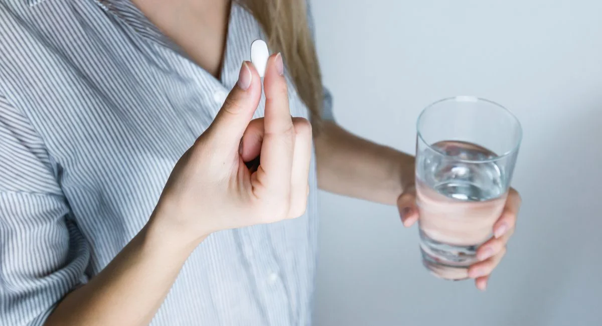 Close-up of a woman holding a pill and a glass of water, ready to take medication.