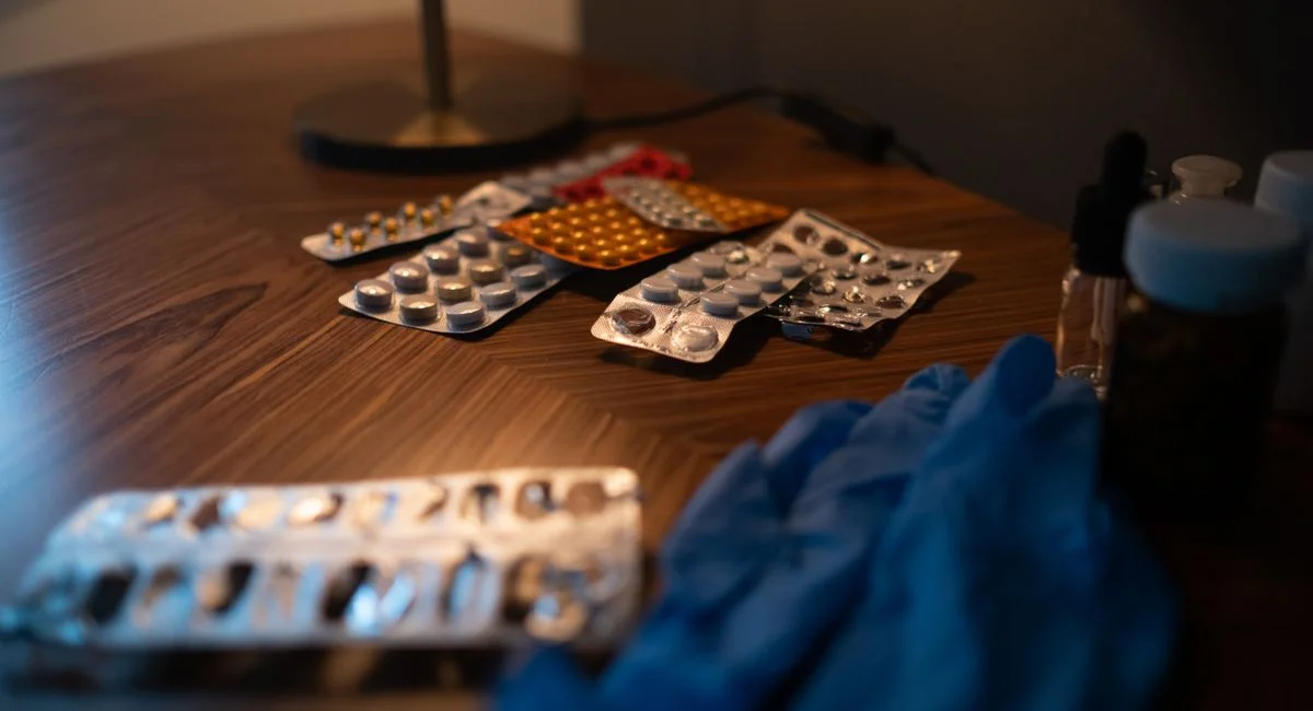 Close-up of various medication blister packs and gloves on a wooden table, signifying health and recovery.