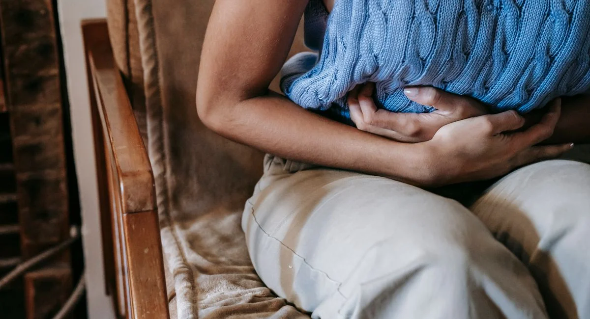 Crop unrecognizable female touching belly while having acute pain in stomach sitting on couch