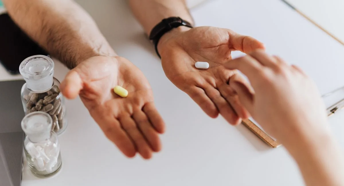 From above anonymous female and unrecognizable doctor man giving yellow and white tablets for choosing while working in moder