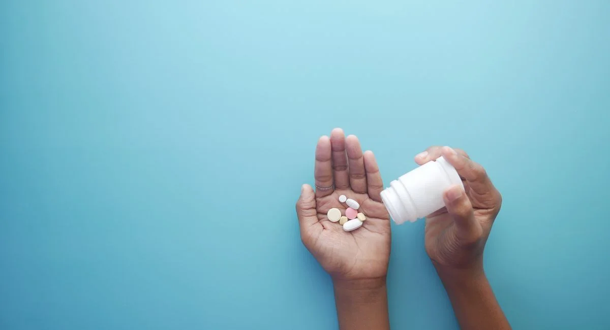 Hands pouring pills from a bottle on a blue background, representing healthcare and medication.