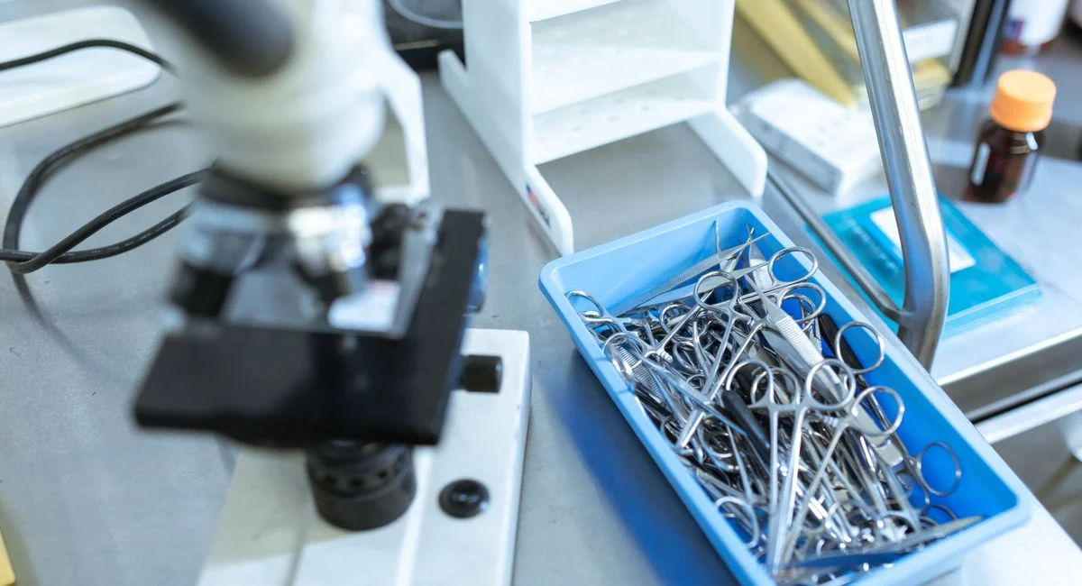 High-angle view of laboratory microscope and tray of medical tools on a lab countertop.