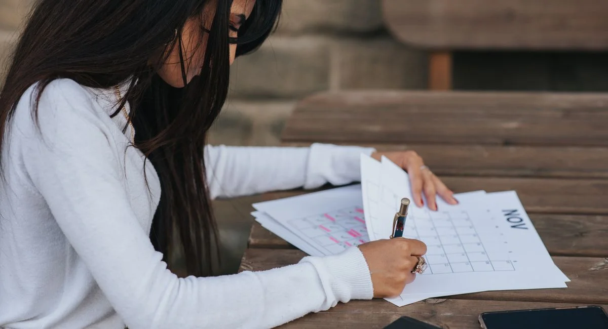 Side view of crop young ethnic female worker writing on paper sheet with month plan while working