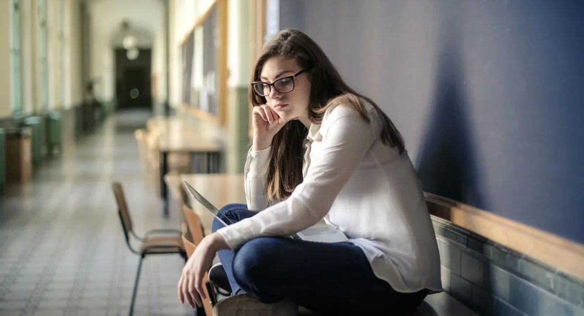 Thoughtful woman sitting alone in a school hallway contemplating problems.