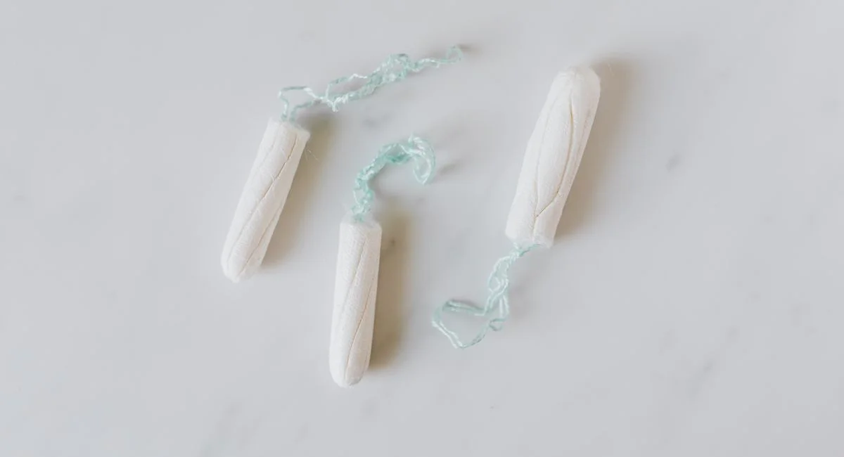 Top view of three hygienic cotton tampons placed on white marble patterned surface